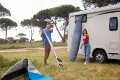 A young couple standing next to their caravan, preparing to go surfing