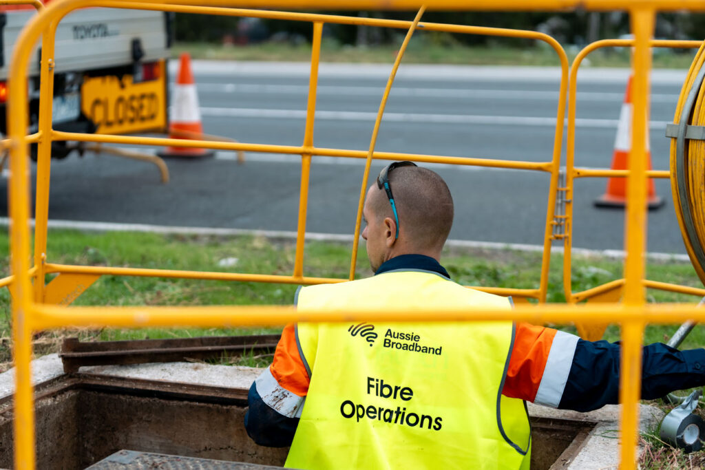 Aussie Broadband worker plugging a fibre cable into 'Fast Streaming Internet' kegs in a cellar