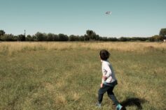 A young boy running across a grassy field, chasing a UFO in the sky