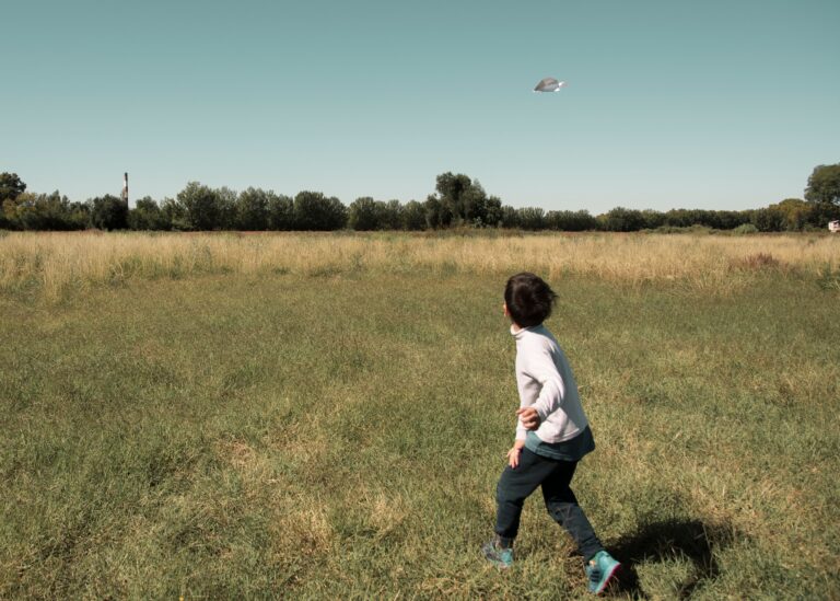 A young boy running across a grassy field, chasing a UFO in the sky