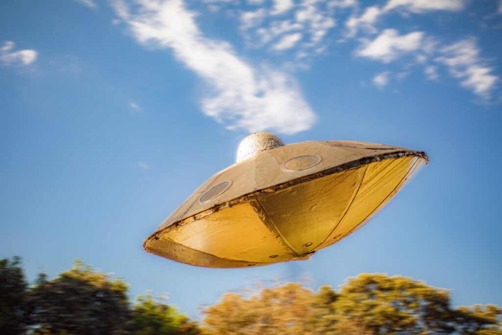 A golden UFO shaped like saucer flying across a blue sky