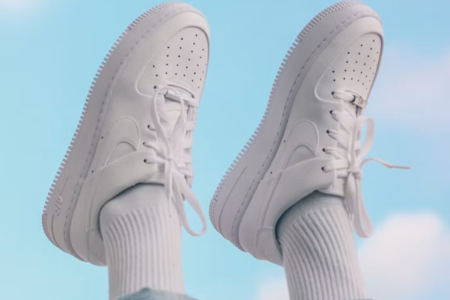 White sneakers with white socks and blue jeans against a blue sky.