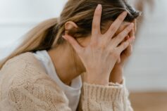 Woman in a beige jumper holding her head in her hands.