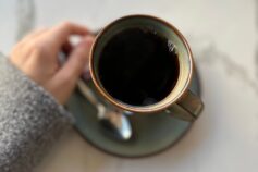 A cup of black coffee on a table, held by a woman