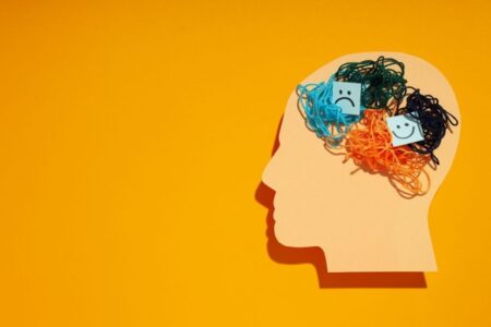 Illustration of a human head silhouette with tangled colourful threads and happy and sad faces, symbolising mental health and emotional wellbeing