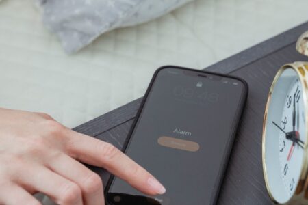 Hand turning off a smartphone alarm beside a bedside clock