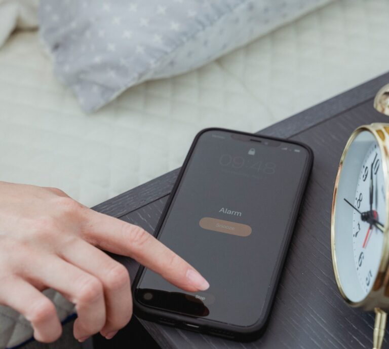 Hand turning off a smartphone alarm beside a bedside clock